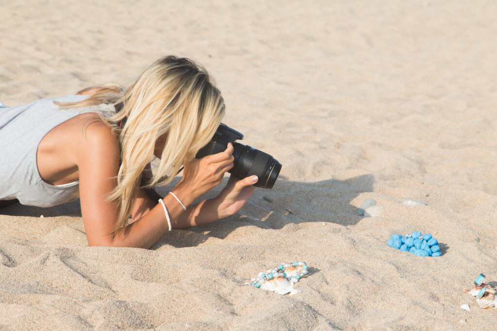 A photographer sets up a jewelry photoshoot on the beach. This photo showcases a content creator, who is one of the five types of remote workers. Content creators make a living by producing digital content, including photography, videos, and written material, to build an audience online. They can work with specific brands or build their own following on social media.